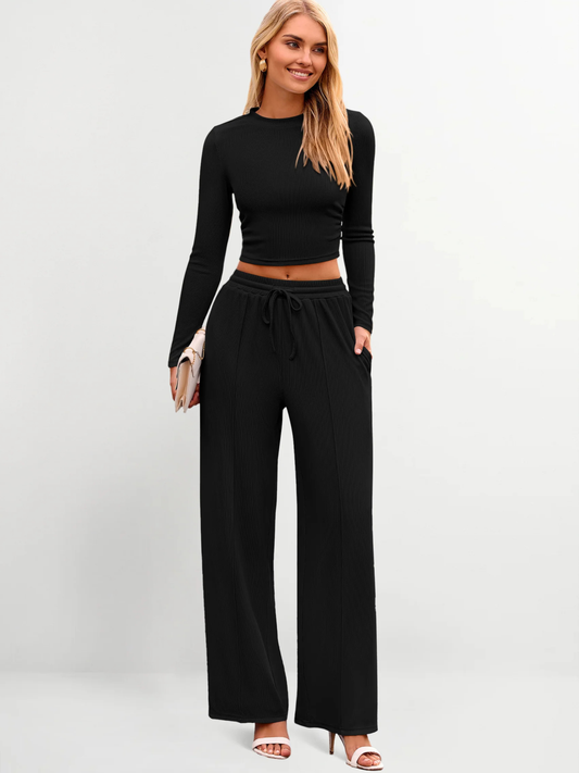 Woman wearing a black long-sleeve top and wide-leg pants on a white background